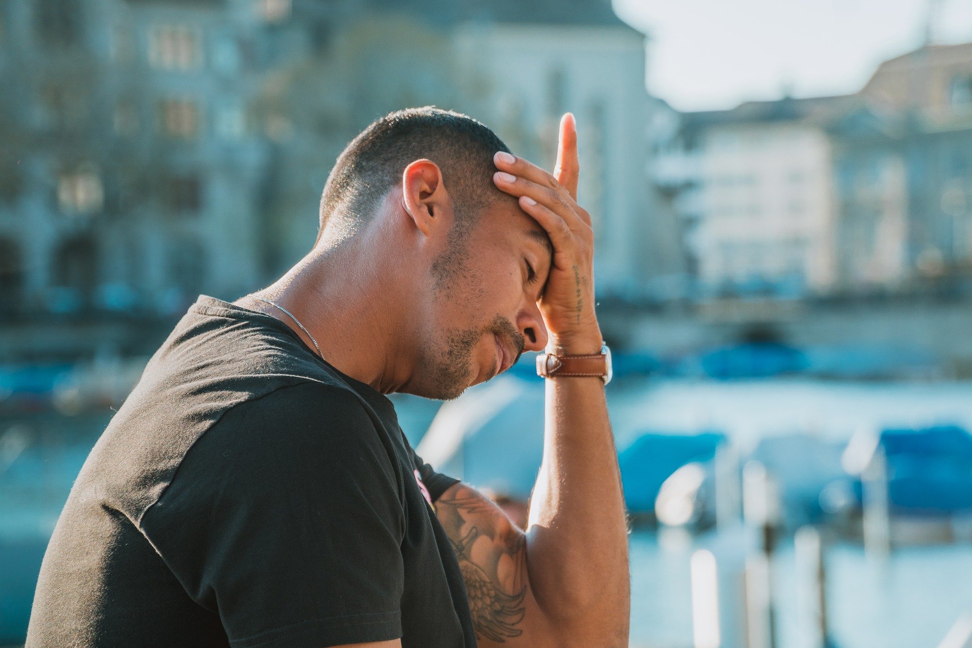 A man sat down outside with his hand on his head, looking upset