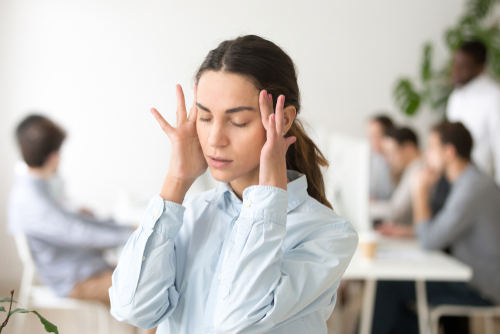 Stressed young woman sat at work with her hands on her head