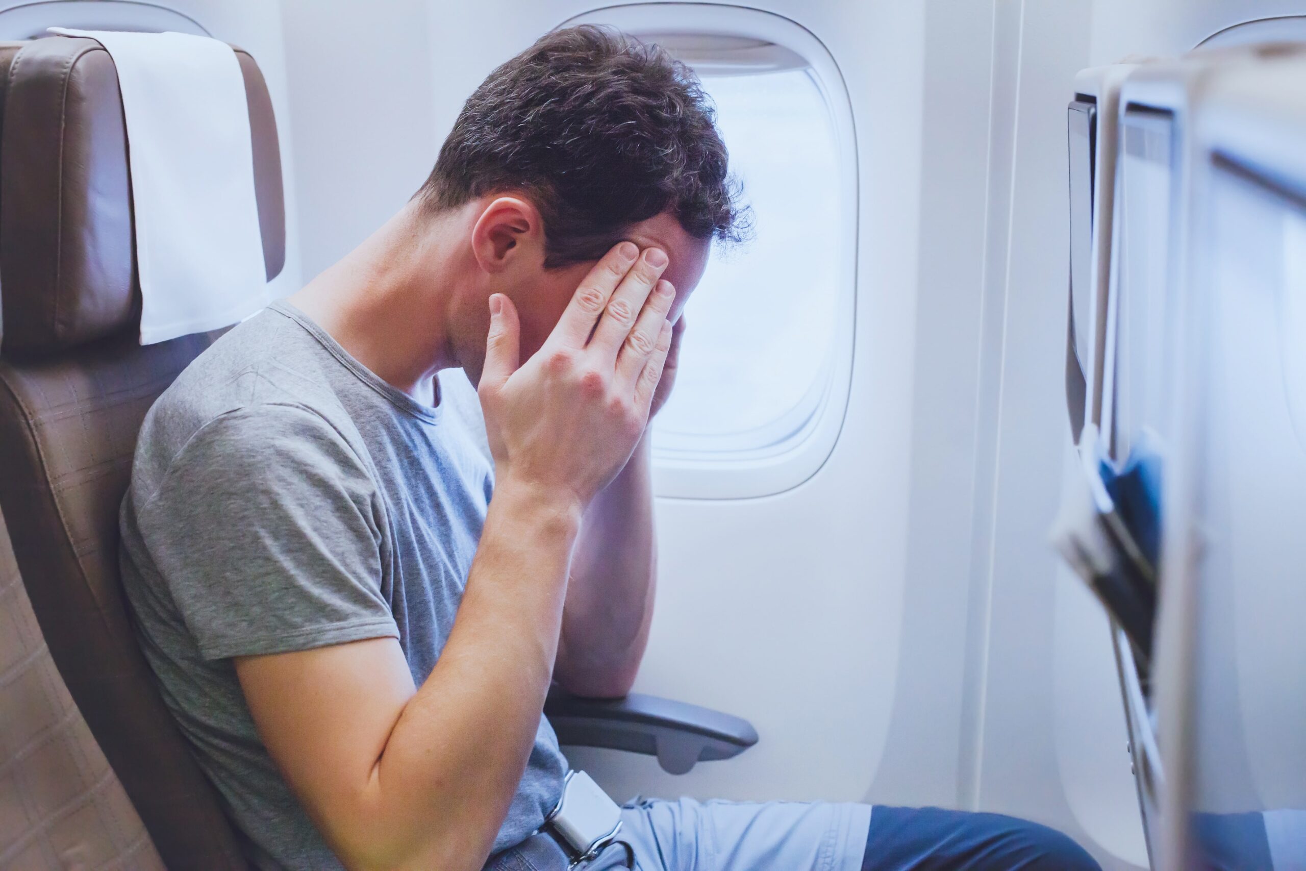 man with fear of flying sat on plane with head in hands