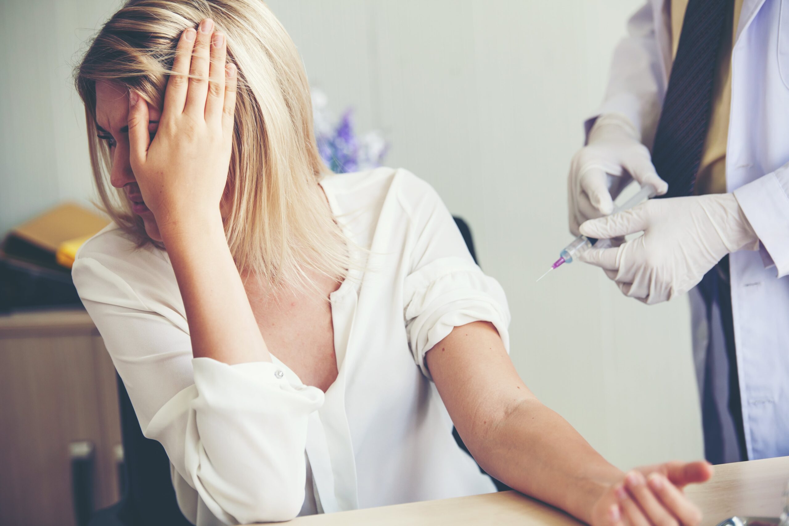 woman with fear of needles covering face while having injection